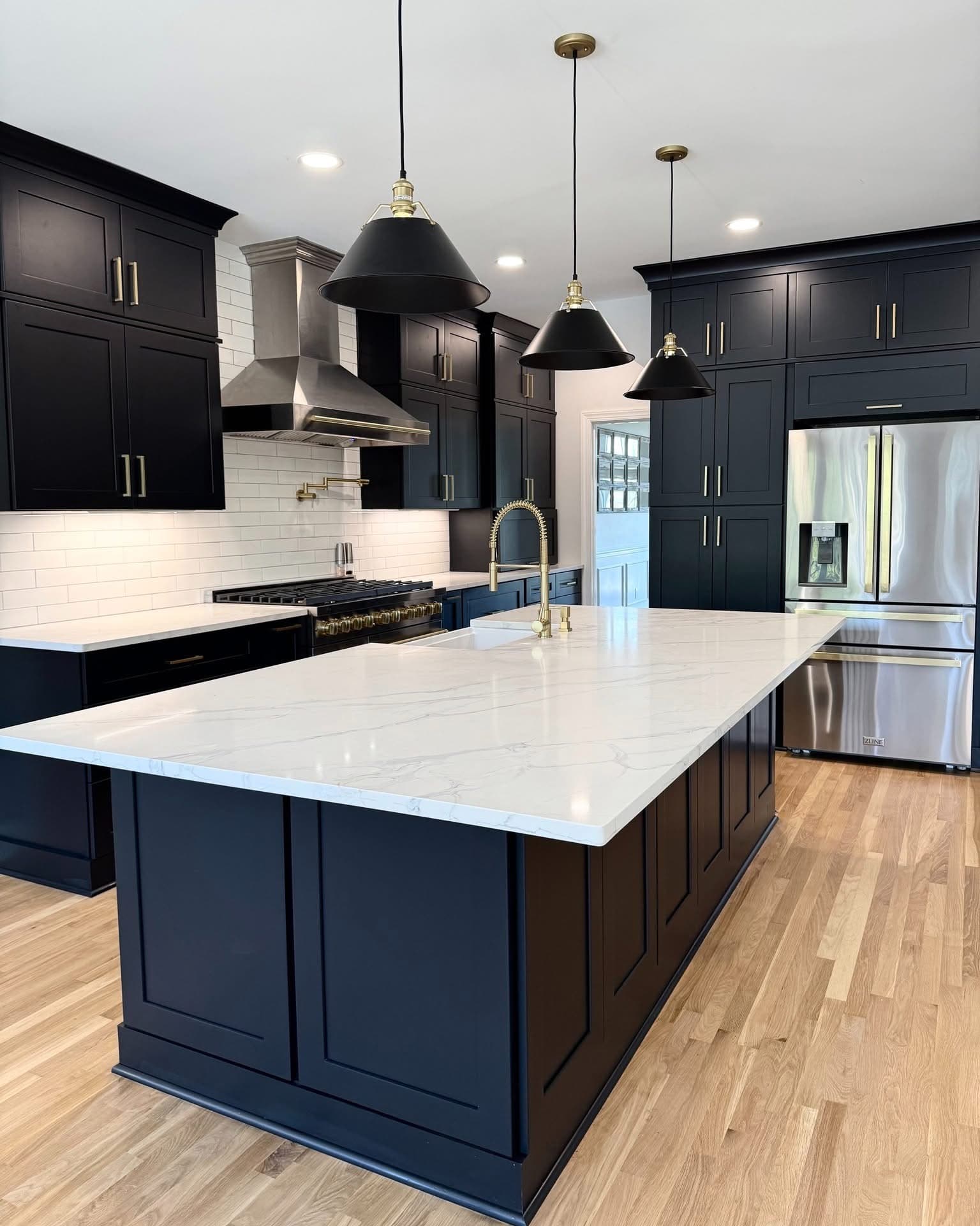 Navy shaker kitchen with a white quartz waterfall island, brass fixtures, and black cone pendant lights.
