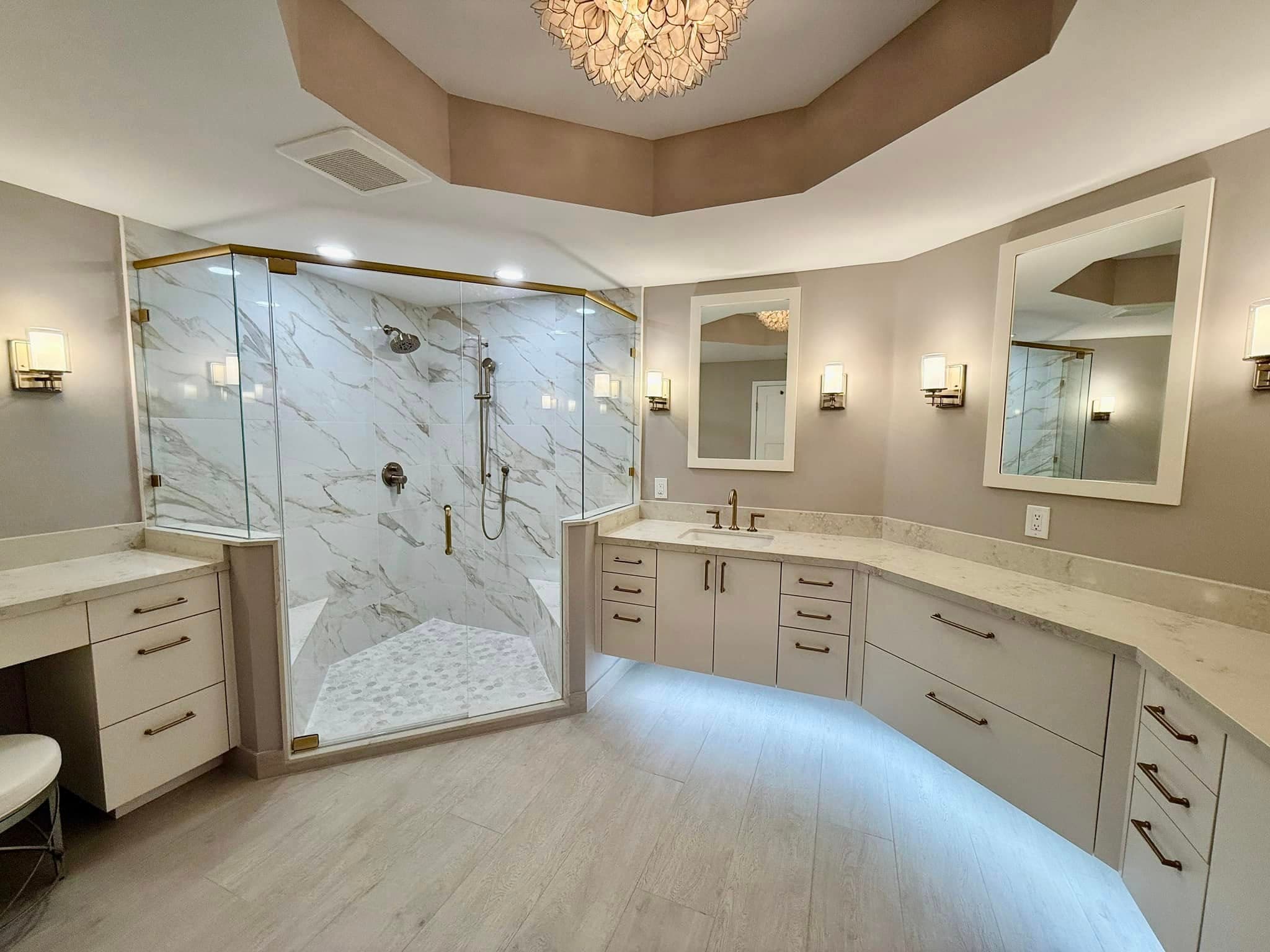 Primary bathroom with a curved vanity, marble-look porcelain, and a frameless glass shower with brass trim.